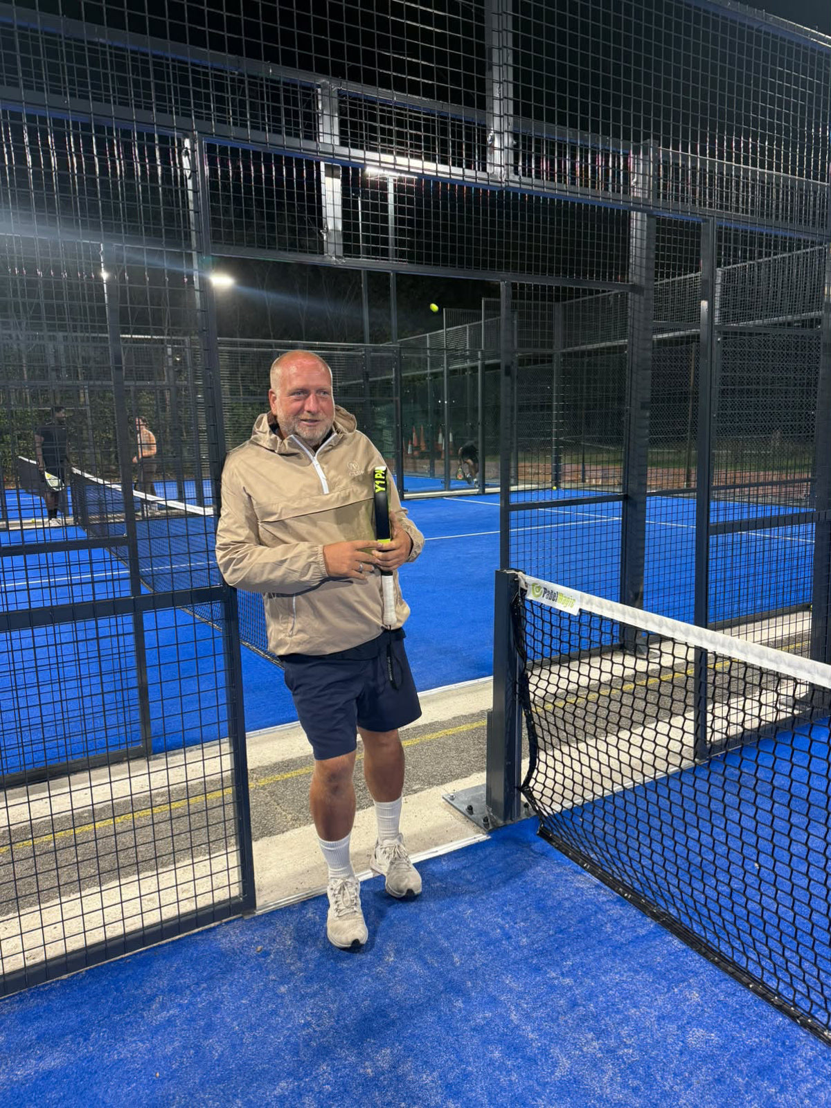 Gary Lowe wearing an AP Club shell beside a floodlit padel court