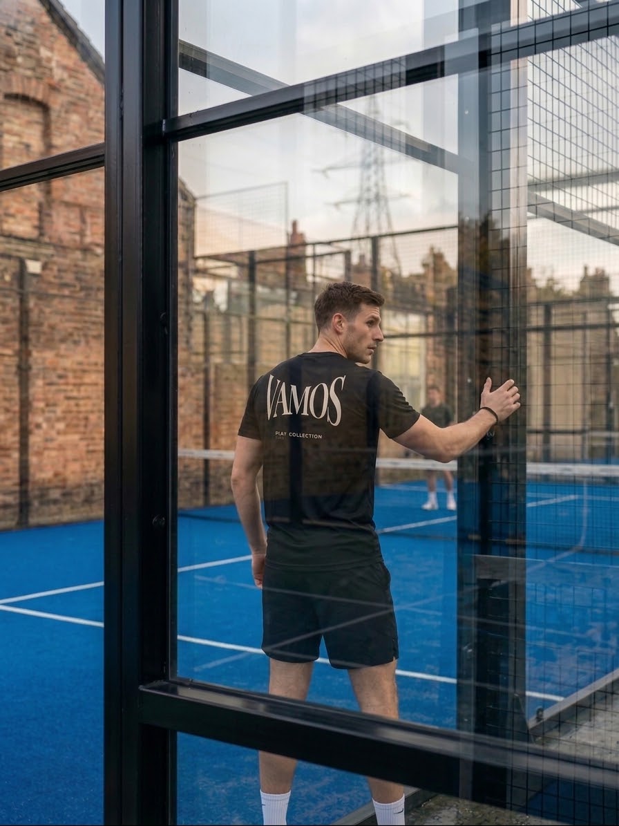 AP Club Vamos Tee worn on a padel court viewed through glass