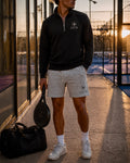 Person wearing a black AP Club Quarter Zip jacket and grey AP Club shorts with a club logo, holding a paddle on a court.