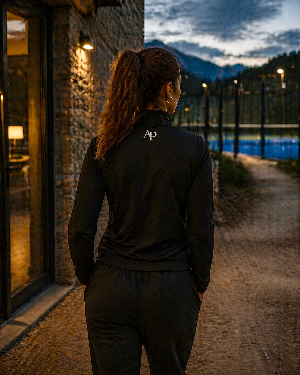 Person wearing a black AP Club Quarter Zip with a logo standing by a building with a view of a lake and mountains.
