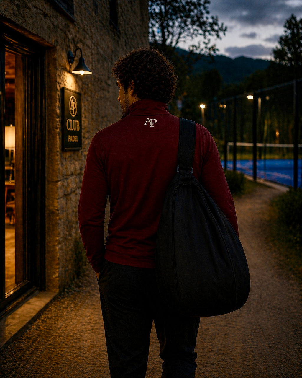 Person with a bag wearing an AP Club Quarter Zip walking towards a padel building at night