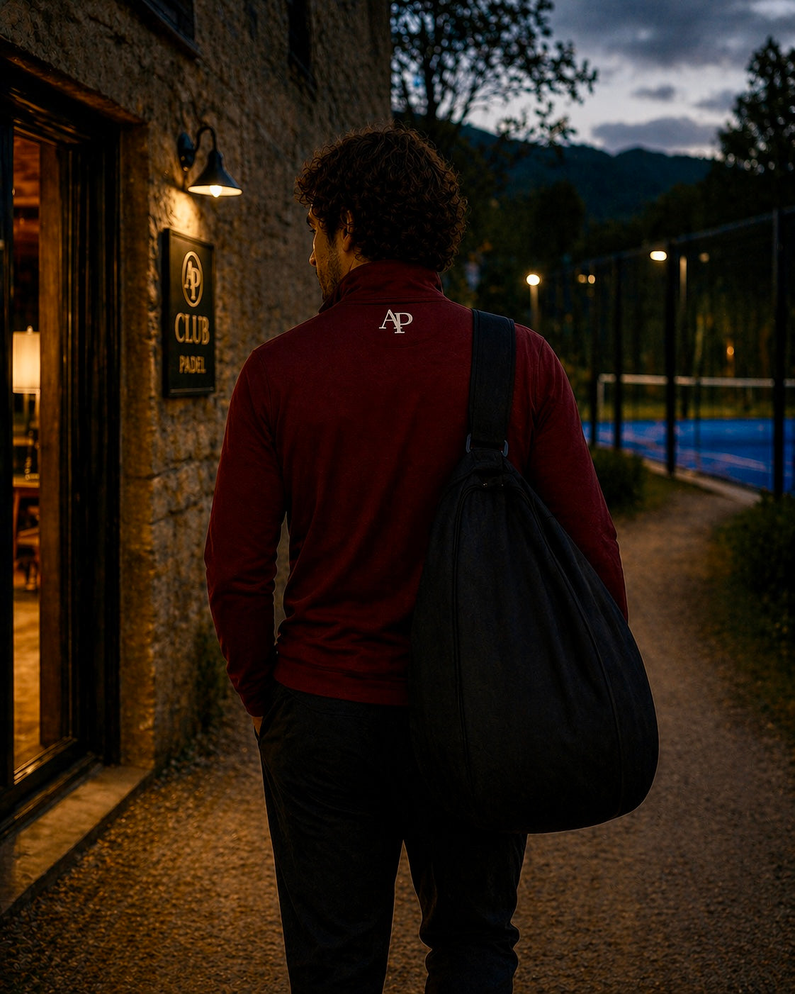 Person with a bag wearing an AP Club Quarter Zip walking towards a padel building at night
