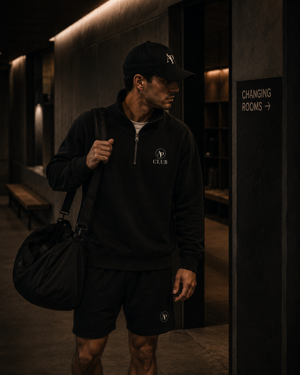 Man in black AP Club quarter zip, black AP Club cap and black AP Club shorts in a padel club.