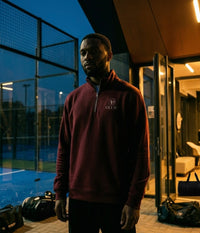 Man wearing a burgundy AP Club quarter zip at a padel club.