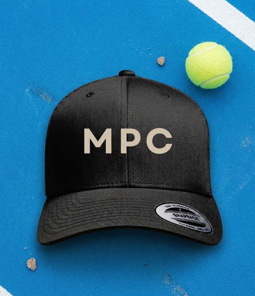 Black cap with 'MPC' logo on a blue surface with a tennis ball