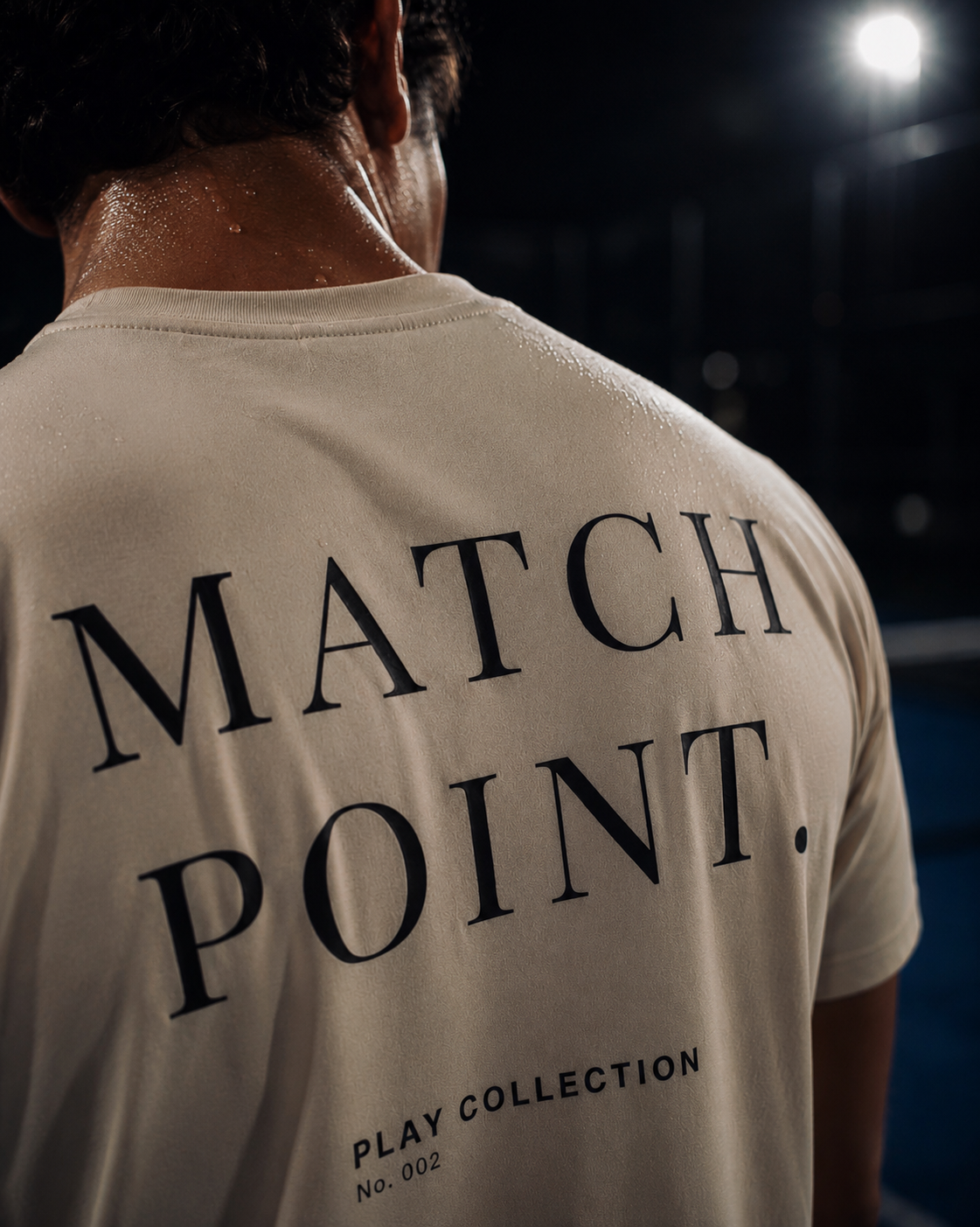 A close-up back view of a padel player wearing a beige AP Club t-shirt with 'MATCH POINT.' printed in black serif text on the back, with 'PLAY COLLECTION No.
